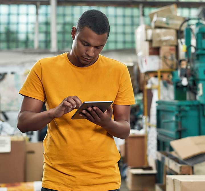 A male SmartSort employee in a distribution center warehouse is performing their job using a mobile tablet device.