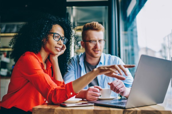 Woman seated at laptop pointing to screen with coworker seated next to her