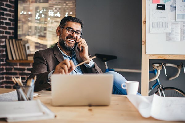 Man sitting in front of laptop while on his cell phone