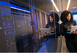 Woman in a black dress working on a laptop standing near servers