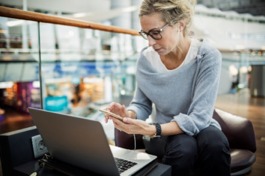 Woman in light blue dress working on her mobile while connected to her laptop