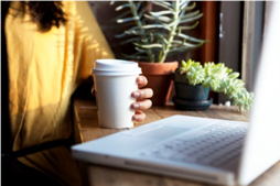 Woman working on her laptop and holding her coffee cup